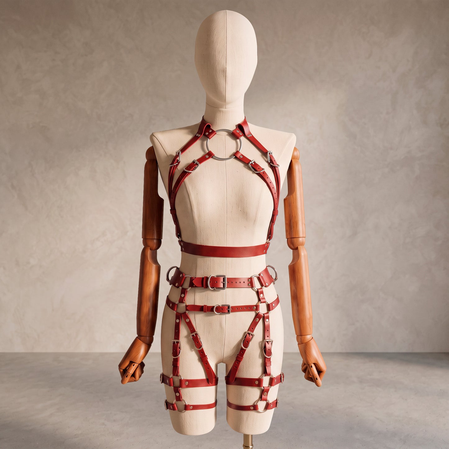 Front view of a deep red leather full body harness set with an open bust harness, open crotch garter belt, removable leather handle, large front ring, adjustable straps, and gold-tone metal hardware.