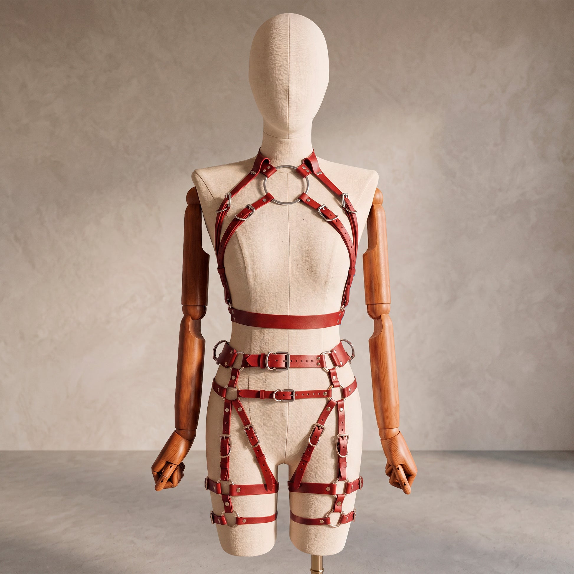 Front view of a deep red leather full body harness set with an open bust harness, open crotch garter belt, removable leather handle, large front ring, adjustable straps, and gold-tone metal hardware.
